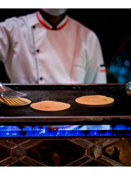 A chef flips delicate, thin crepes or chilas on a hot griddle. This action shot highlights the skill and dexterity of our culinary team in preparing a wide range of dishes live.