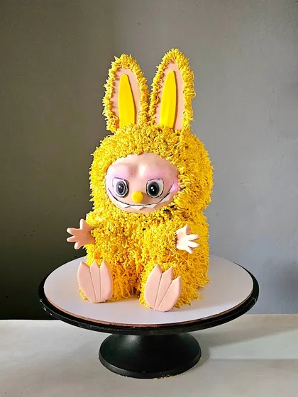 This fully 3D sculpted cake brings the popular character Labubu to life. Instead of just a topper, the entire cake is shaped into the character, complete with fluffy yellow "fur" made from buttercream. This type of structural cake requires a different level of artistry and is a true showstopper.