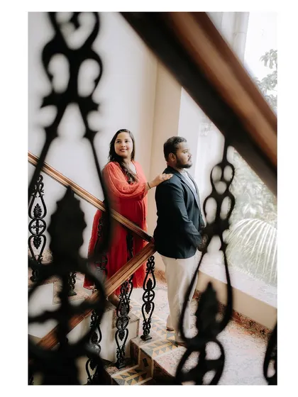 Using the intricate railing of a staircase to frame the couple adds depth and artistry to this indoor portrait.