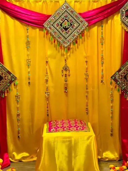 For this home ceremony, I used a combination of bright yellow and rich pink drapes. The backdrop is decorated with traditional Gujarati torans and mirror work hangings, creating a rich, ethnic look for the function.