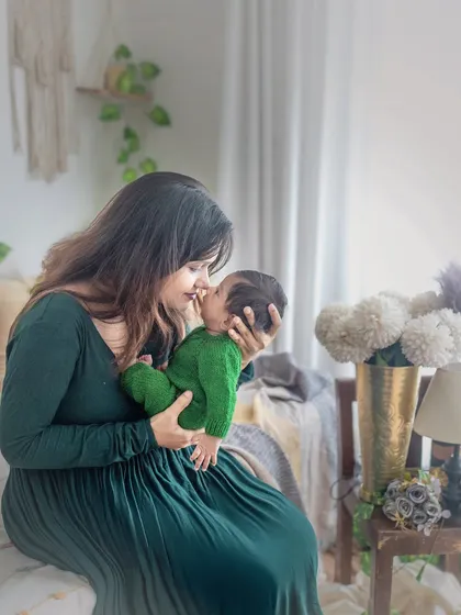A mother and her two-month-old baby share a quiet moment in my boho-themed studio. The natural window light, earthy green tones, and macrame details create a calm and serene atmosphere for lifestyle portraits.