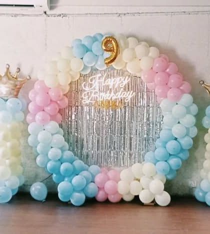 A royal pastel theme for a 9th birthday. This circular balloon arch in soft pink, blue, and cream is set against a silver fringe curtain. I added balloon columns topped with gold crowns to make the birthday child feel like royalty.