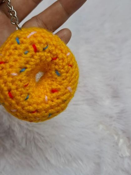 A delicious-looking donut keychain. This amigurumi treat is crocheted in a golden yellow "dough" color and topped with colorful embroidered "sprinkles."