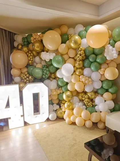 We created this elegant balloon wall for a 40th birthday party. The organic arrangement of green, white, and gold balloons pairs beautifully with the large light-up marquee numbers for a sophisticated celebration.
