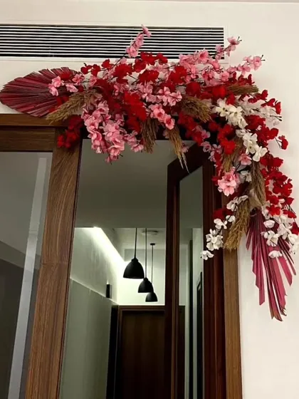 A stylish and modern floral swag over a doorway, using a mix of red and pink flowers with dried palm leaves.
