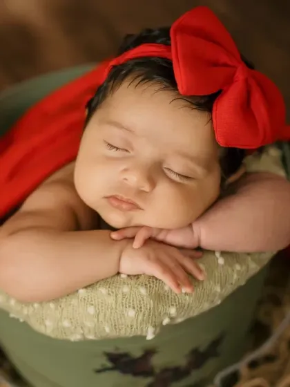 This portrait captures the baby's peaceful expression and the soft texture of the red wrap and bow.