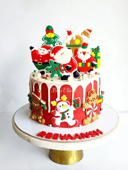 A Christmas-themed birthday cake for Reevaansh. This festive red cake is adorned with edible Santas, gingerbread men, and Christmas trees.