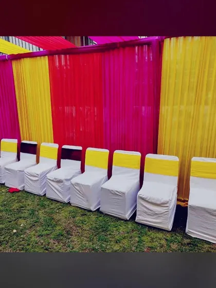 We provide all necessary seating for guests. This row of chairs is neatly arranged with white covers and yellow sashes, matching the yellow and pink theme of the Mehandi decor.