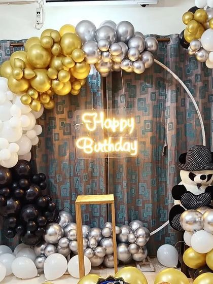 A chic black, white, gold, and silver balloon ring backdrop for a birthday party, complete with a cute panda detail and a bright neon sign.