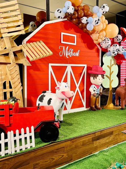 Welcome to Mikhail's barnyard birthday. This large-scale setup features a big red barn, a wooden windmill, and life-sized cutouts of a cowboy, cow, and horse, creating an immersive farm experience.