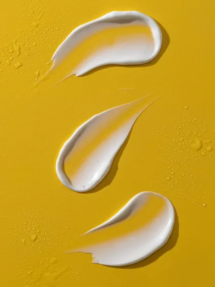 A macro shot of three perfect skincare cream smears on a bright yellow background. The lighting highlights the glossy texture and subtle shadows, creating a visually satisfying image that speaks to the product's quality.