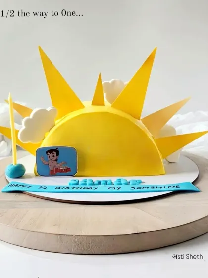 A "halfway to one" celebration cake shaped like a rising sun, featuring the beloved cartoon character Chhota Bheem.