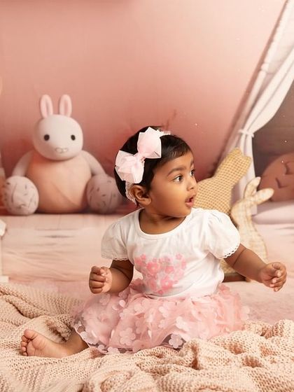 A curious glance in a world of pink. This toddler portrait captures a candid moment as the little girl looks off to the side, surrounded by her bunny-themed room.