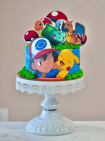 Gotta catch 'em all. This Pokémon-themed cake is perfect for any fan, featuring Ash, Pikachu, and other favorite characters as edible toppers on a vibrant blue and green cake.