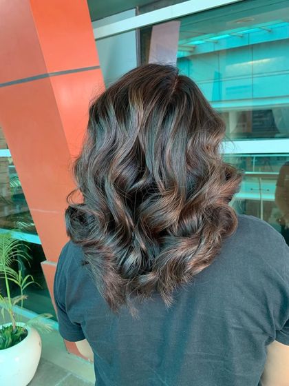 This image shows a beautiful example of a subtle balayage on medium-length dark hair. The soft, light-brown highlights are blended seamlessly to create depth and are styled in loose waves for a relaxed, elegant finish.