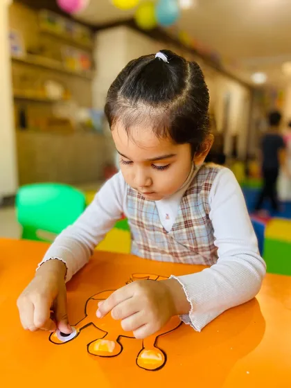 A girl in a plaid vest carefully assembles her paper craft, demonstrating great concentration.