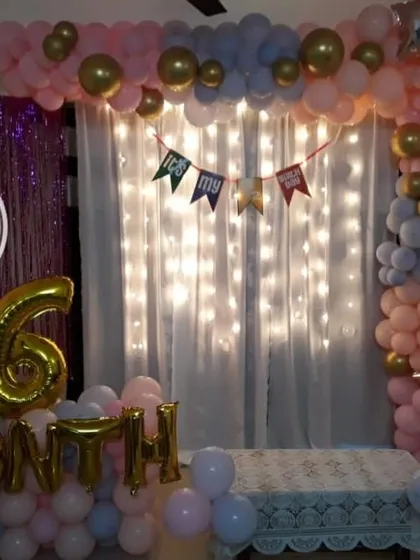 A sweet 6-month celebration setup at home, with a backdrop of fairy lights, a pink and blue balloon arch, and foil balloons marking the milestone.
