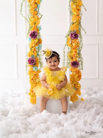 A first birthday portrait that feels like a dream. This sweet baby girl is surrounded by clouds and a beautiful floral swing, creating a whimsical and joyful scene to mark her special day.