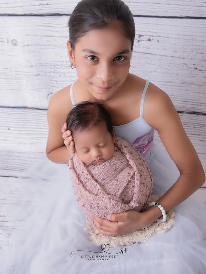 A proud big sister holds her swaddled baby brother. I guide older siblings to hold the baby safely and comfortably, resulting in a portrait that is both beautiful and secure.