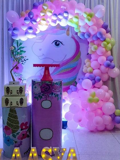 A unicorn-themed backdrop with a beautiful balloon arch in shades of purple and pink, ready for a cake table setup.