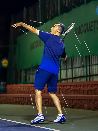 A player executes a powerful serve during a night match. Our floodlit courts allow you to play your best game even after the sun goes down.