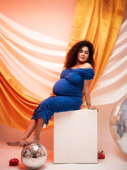 A bold and vibrant studio portrait. The electric blue dress, disco balls, and colorful backdrop create a fun and modern vibe for this maternity shoot.