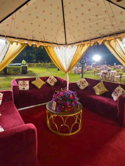 A luxurious cabana seating area for the Sufi Sangeet. The deep red velvet sofas, custom-printed cushions, and elegant tent create a cozy and royal lounge space for guests.