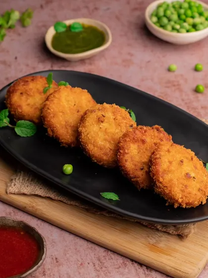A platter of crispy vegetable patties served with green chutney. The dark plate makes the golden-brown patties stand out.