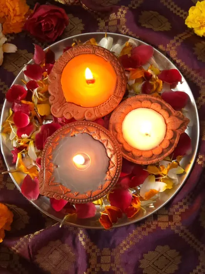 A trio of my tri-color Diya Candles lit and arranged on a traditional silver plate with flower petals. This image captures the sacred energy and celebratory spirit they bring to any space.