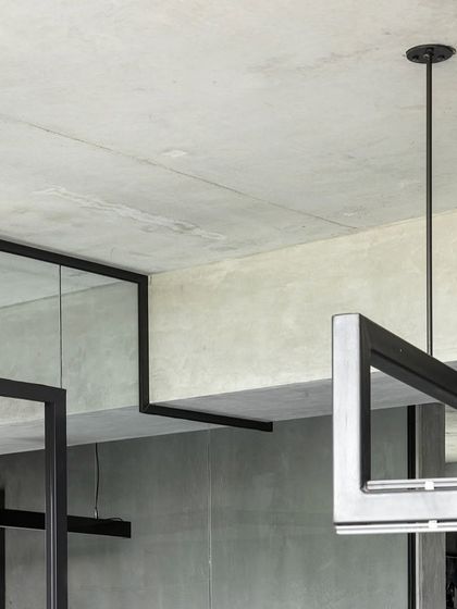 A detail of the structural and lighting elements in our studio. The exposed concrete ceiling and black steel framing create a raw, industrial feel, reflecting our honest approach to materials and construction.