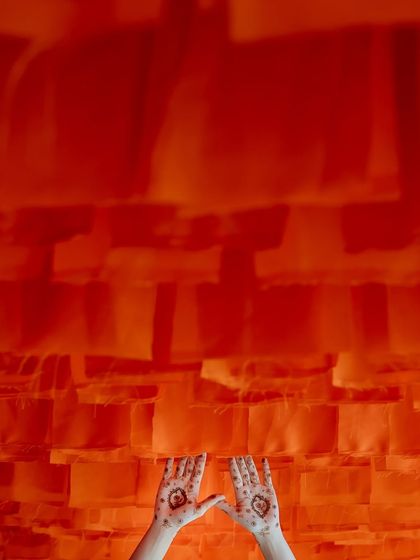 An artistic shot of the bride's henna-adorned hands against a vibrant orange backdrop.