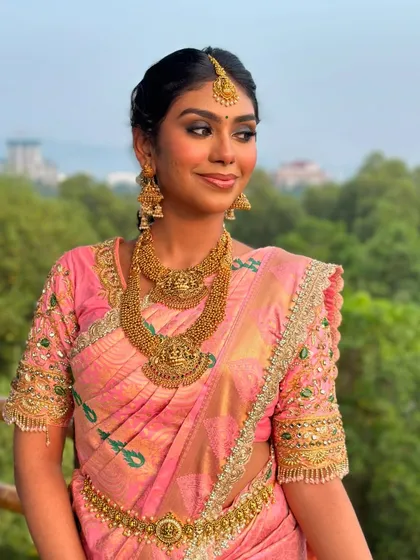 A beautiful smile that lights up the frame. This South Indian bridal look features a soft smokey eye and radiant skin, perfectly complementing her pink Kanjeevaram saree and temple jewelry.