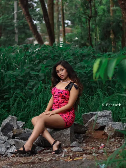 A seated portrait of the model in the pink dress, set against a lush green, natural background. This contrasts the edgy dress with a softer environment.