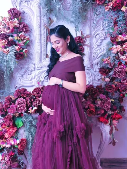 A solo portrait of the mother-to-be, glowing amidst a stunning floral arch. This setup uses a variety of deep red, purple, and pink flowers to create a rich, textured backdrop that makes for unforgettable pregnancy photos.