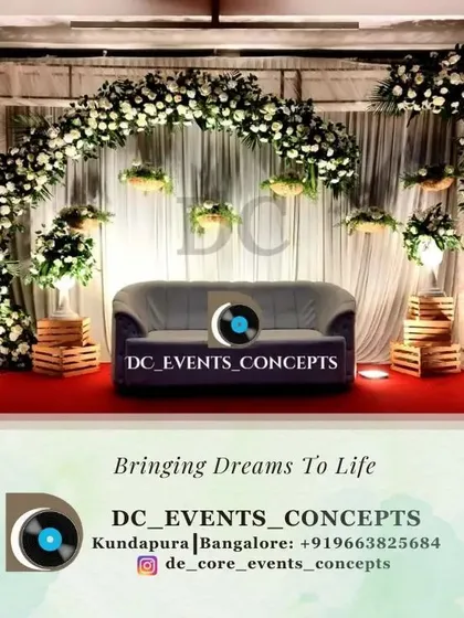 This reception decor features a graceful arch of white flowers against a simple draped backdrop. The minimalist design is enhanced by warm uplighting, creating a chic and intimate setting.