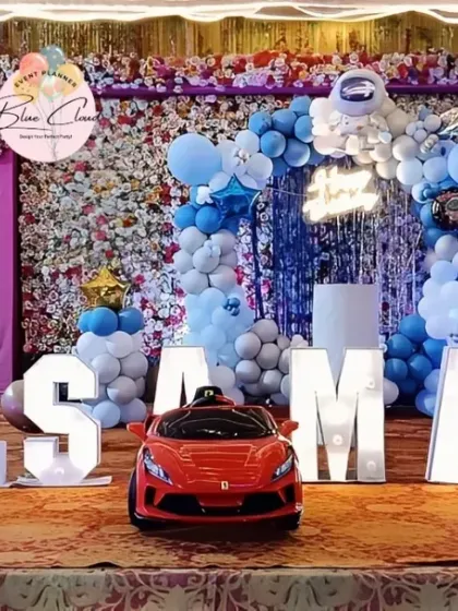 A full stage setup with marquee letters, a balloon arch, and a toy car for a first birthday.
