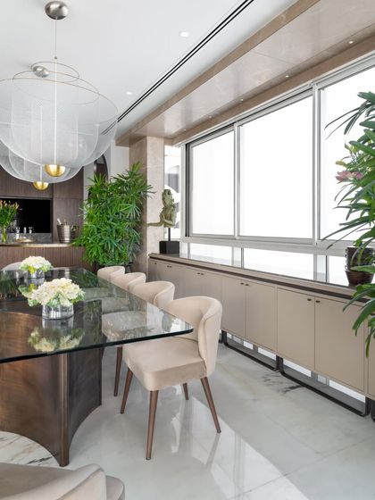 This angle highlights the custom credenza along the window, providing ample storage for the dining area. The space is filled with natural light, and lush green plants add a touch of life and freshness to the elegant setting.