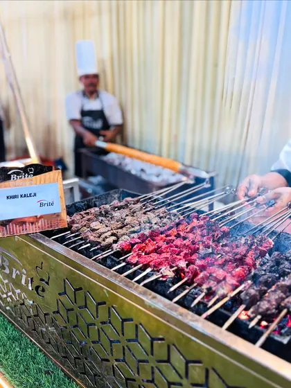 The Khiri Kaleji barbecue station, where skewers of marinated meat are grilled over live coals, with a chef working in the background.