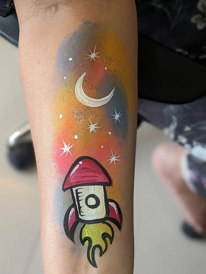 A fun rocket ship tattoo, blasting off into a colorful, starry galaxy on the arm.