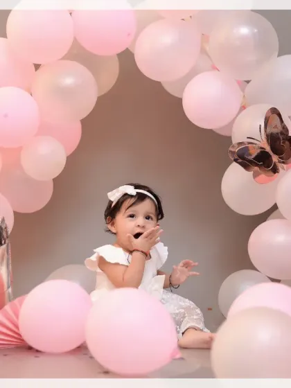 A sweet baby girl surrounded by a beautiful arch of pink balloons. This setup is perfect for creating soft and dreamy milestone portraits.