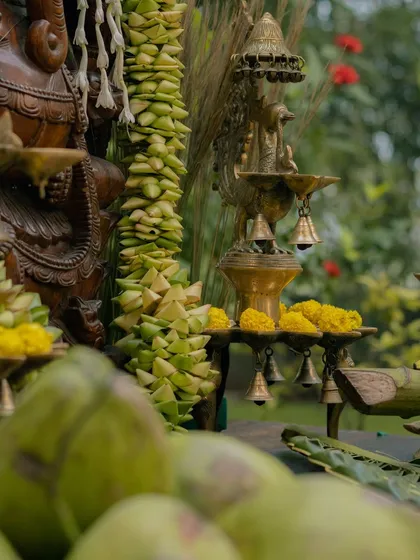 The warm glow of brass temple lamps, or 'diyas', adds a sacred ambiance. Here, they are placed alongside woven palm leaves and marigolds as part of the traditional decor.