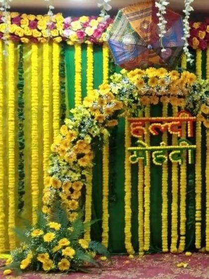 A combined "Haldi Mehandi" backdrop with a floral arch made of sunflowers and marigolds. The green and yellow drapes are complemented by Rajasthani umbrellas, creating a vibrant and traditional look.