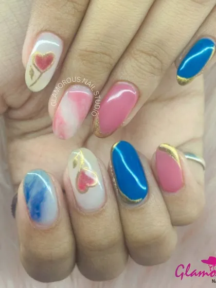 A playful and artistic mix of designs. This set includes nails with a blue and white marble effect, pink and gold accents, and a hand-painted heart design, showing how we can combine different styles into one cohesive look.