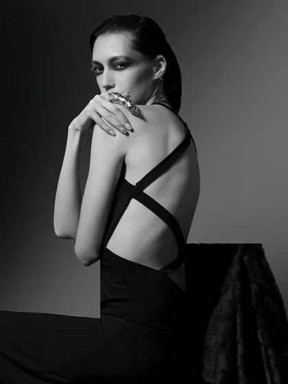 A classic black and white fashion portrait. The dramatic lighting, cross-back dress, and the model's intense gaze create a timeless and powerful image.