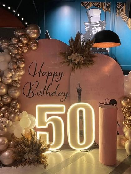 A closer look at the elegant 50th birthday decor. The warm glow from the neon numbers and the metallic sheen of the rose gold balloons create a warm and inviting atmosphere.