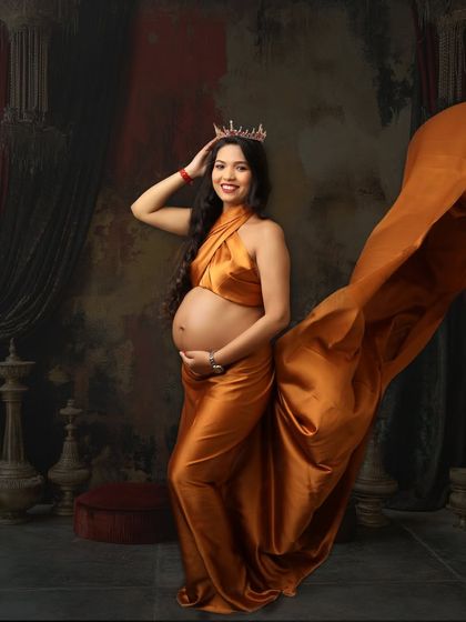 A powerful pose showing off the baby bump in a flowing golden satin wrap. The crown and regal backdrop highlight the queenly essence of every expecting mother.