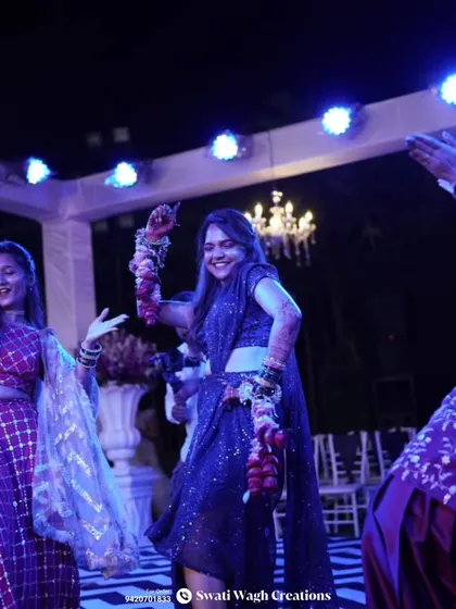 The bride is having fun on the dance floor during her sangeet. Her deep red floral kalire, made with rose petals, add a dramatic flair to her navy blue saree.