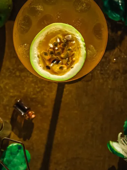 A top-down shot of the passion fruit drink, using dramatic shadows and a single light source to highlight the vibrant color and garnish.