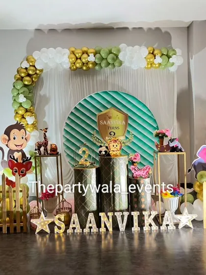 A fun jungle theme with a green and white balloon arch. The setup includes gold pedestals and cute monkey and lion cutouts.