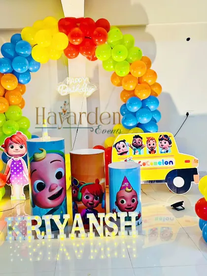 This Cocomelon setup features the iconic yellow school bus cutout. The bright primary-colored balloon arch and character plinths create a playful atmosphere for a toddler's birthday party.